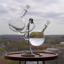 Load image into Gallery viewer, Glass water sculpture on a wooden table with a cityscape background
