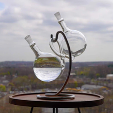 Load image into Gallery viewer, Glass SyphonAir with water on a stand against a cityscape background

